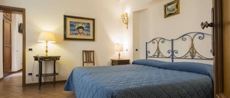A bedroom with a bed, a chair, a table, a lamp, and a wall-mounted picture.