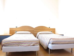 Zwei Einzelbetten mit Holz Kopfteilen und gestreifter Bettwäsche in einem Zimmer mit Holzboden und einem Nachttisch mit Lampe.