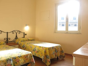 Una habitación con dos camas, una ventana y una lámpara fijada a la pared.
