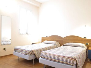 Ein Hotelzimmer mit zwei Betten, einem Holzkopfteil, einem Nachttisch und einem Wandspiegel sowie einem Fenster.