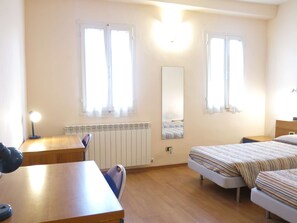 A room with two beds, a desk, a chair, a radiator, and a mirror. - Apartment in Piazza del Campo area 3 bedrooms 2 bathrooms (siena)