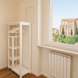 A corner room with a white built-in wardrobe, a radiator, and a window with a view of a building. - Top Floor - Top Location (Siena)