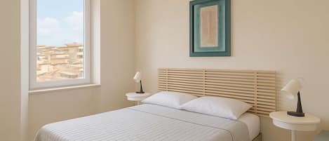 A bedroom with a bed, bedside tables, a window, and a framed picture on the wall.