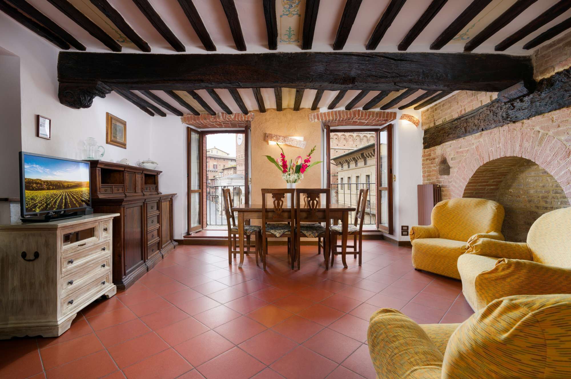 A room with a wooden table, chairs, a television, and a sofa.