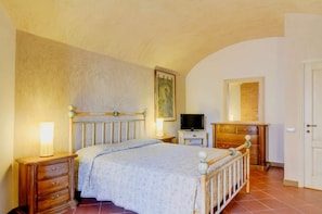 A bedroom with a bed, bedside tables, a television, a dresser, and a door. - A BALCONY ON THE PIAZZA OF THE PALIO (Siena)
