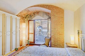 Ein Schlafzimmer mit einem Bett, einem Sessel, einem Kleiderschrank und einem Balkon mit Blick auf die Straße.
