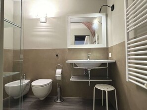 A modern bathroom with a glass shower enclosure, a toilet, a bidet, a sink with a mirror above, and a towel rack. - Very Central Studio close to public parking and il Campo (Siena)