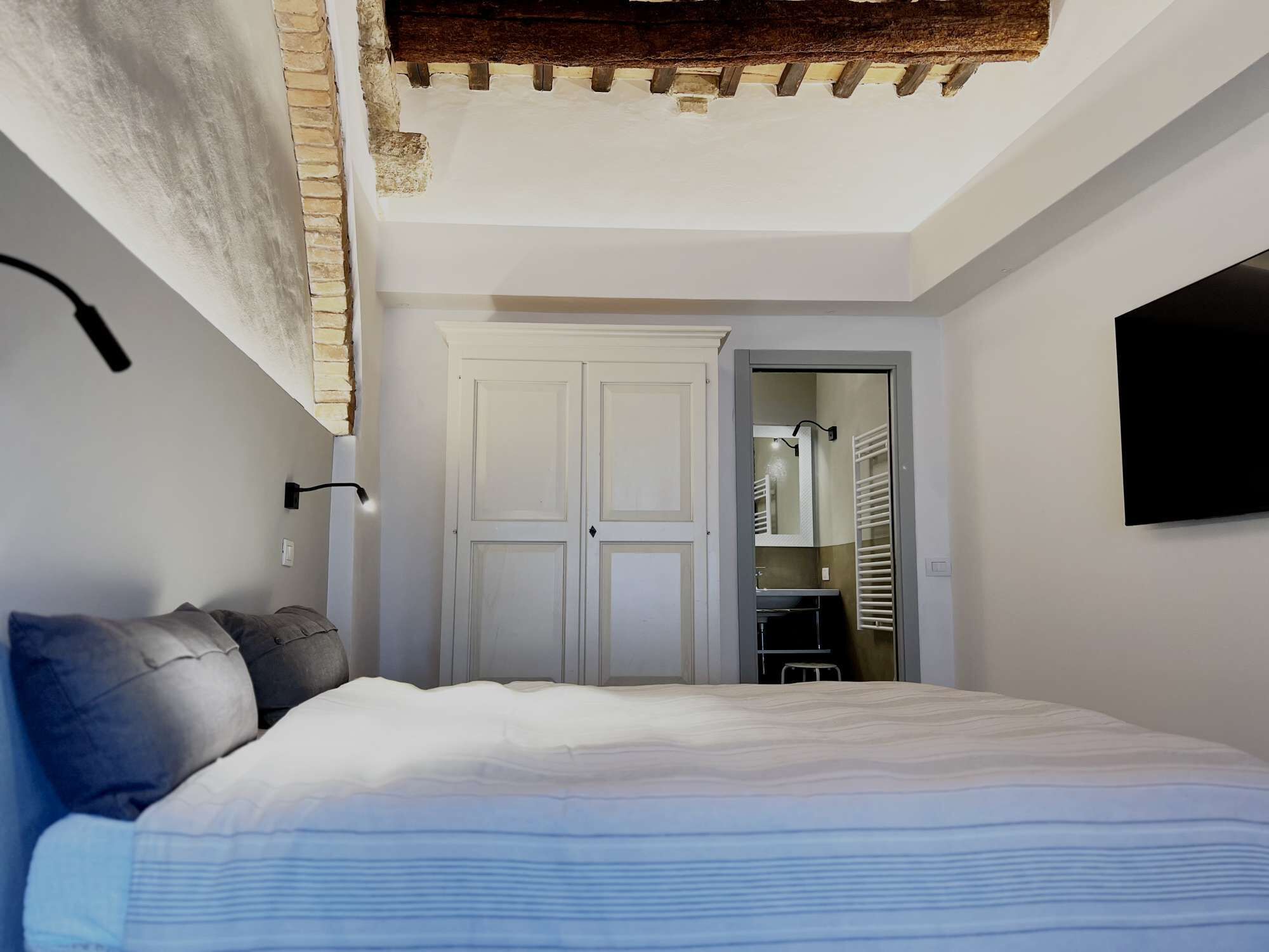 A bedroom with a bed, a wardrobe, a mirror, and a television mounted on the wall.