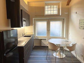 A compact kitchen with a dining area, a window with frosted glass, and a wall-mounted light fixture. - Very Central Studio close to public parking and il Campo (Siena)