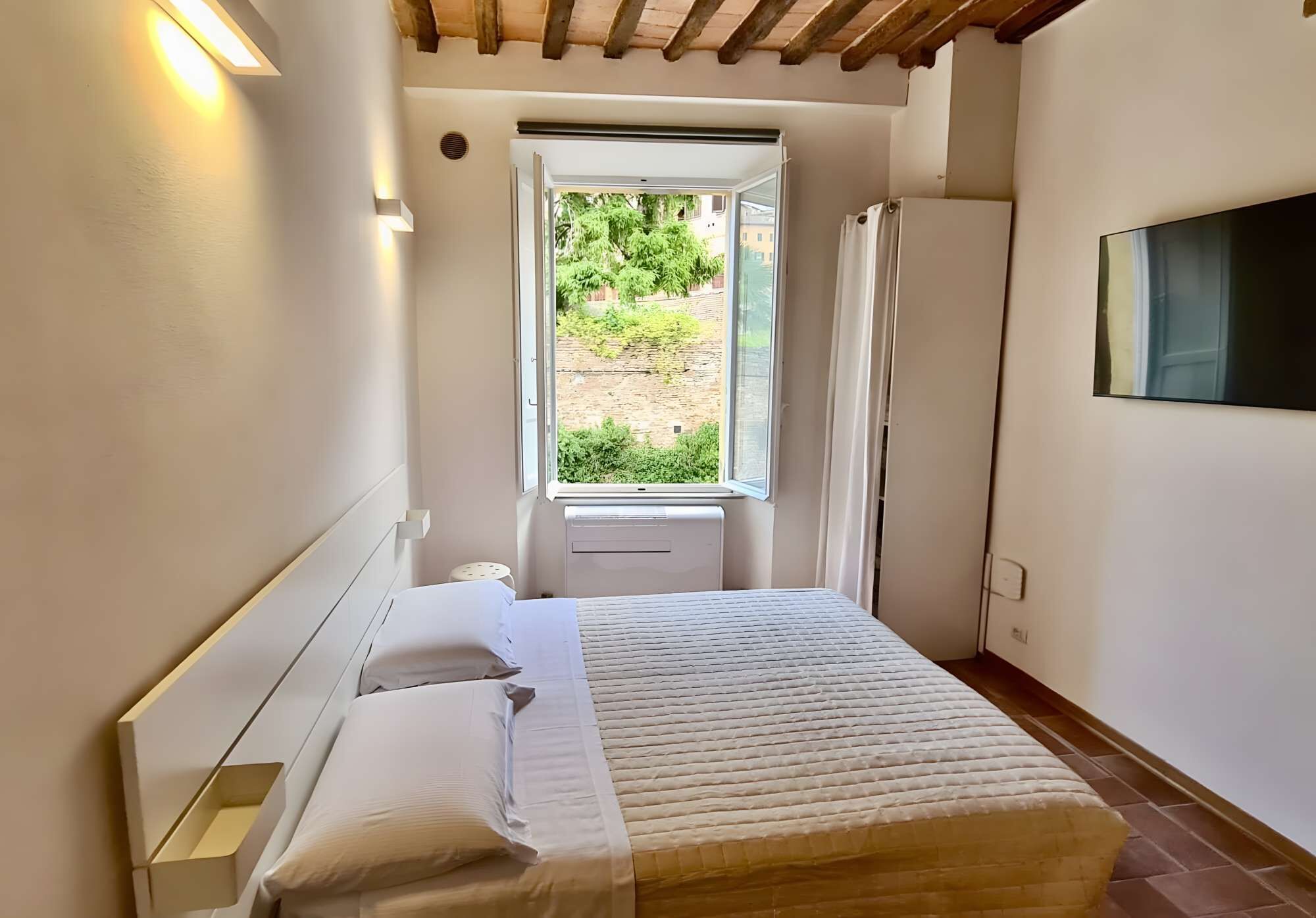 A bedroom with a bed, a window, a TV, and a ceiling fan.