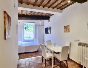 A compact room with a bed, a dining table with chairs, a radiator, and a window with a view of greenery. - Very central studio II close to public parking and il Campo (Siena)