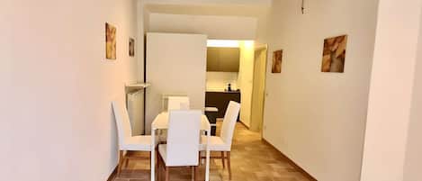 A dining area with a table and chairs, a kitchen in the background, and a wooden ceiling.