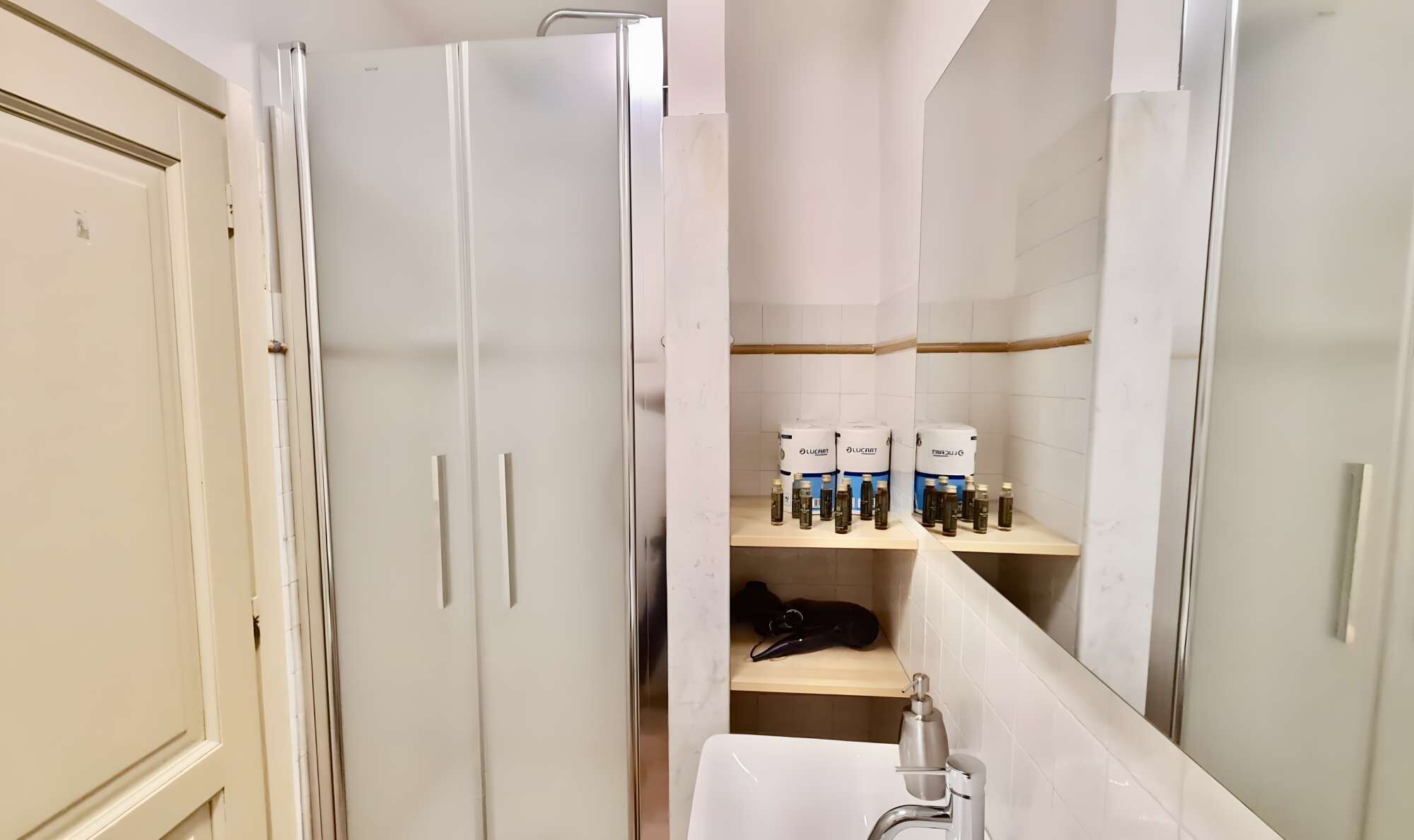 Une salle de bain avec un lavabo blanc, un miroir et des étagères remplies de flacons de produits de toilette.