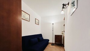 A room with a dark blue sofa, a floor lamp, and two framed pictures on the wall. - A BALCONY ON THE PIAZZA OF THE PALIO (Siena)