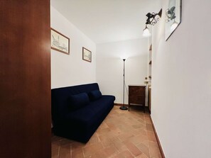 Ein Zimmer mit einem dunkelblauen Sofa, einer Stehlampe und zwei gerahmten Bildern an der Wand.