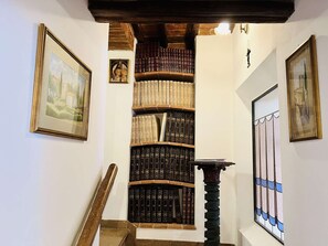 A staircase with a bookshelf filled with books, framed artwork on the walls, and a stained glass window. - A BALCONY ON THE PIAZZA OF THE PALIO (Siena)