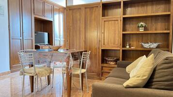Un soggiorno con un divano marrone, un tavolo da pranzo con sedie, mobili contenitori in legno e un televisore.