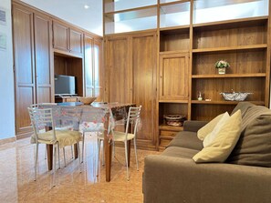 Ein Wohnzimmer mit braunem Sofa, einem Esstisch mit Stühlen, Holzschränken und einem Fernseher.