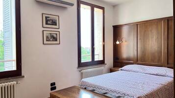 Un dormitorio con una cama, un armario de madera, dos cuadros enmarcados en la pared y una ventana con vistas a la vegetación.