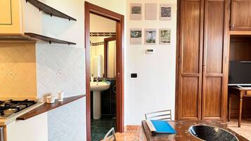 Una cucina con piano cottura a gas, lavello e pensili in legno. Si nota un tavolo da pranzo con sedie e una ciotola decorativa.