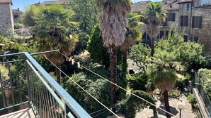 Ein Balkon mit Blick auf einen Garten, einschließlich Palmen und einem Steinhaus.