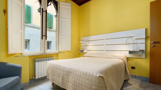 A bedroom with a bed, a radiator, a window with shutters, and a door. - A BALCONY ON THE PIAZZA OF THE PALIO (Siena)