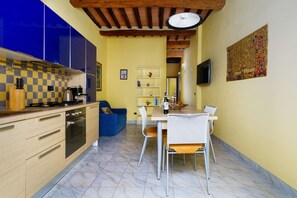 A compact kitchen with modern appliances, a dining area with a table and chairs, and a blue sofa. - A BALCONY ON THE PIAZZA OF THE PALIO (Siena)