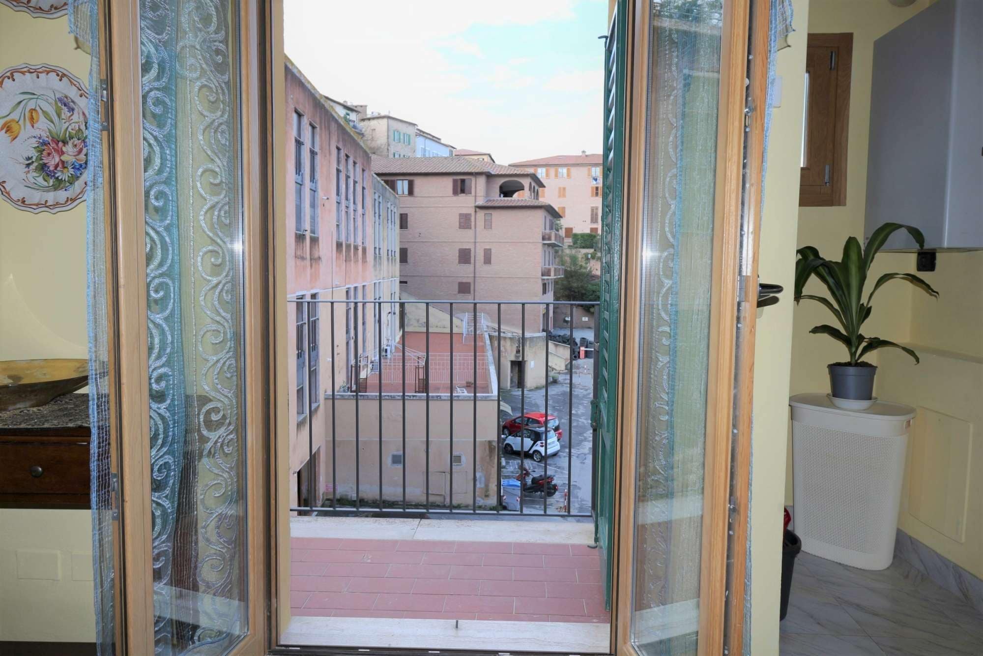 A balcony with a view of a residential street, a potted plant, and a radiator.