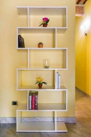 A white shelving unit with multiple compartments, some containing books and plants. - A BALCONY ON THE PIAZZA OF THE PALIO (Siena)