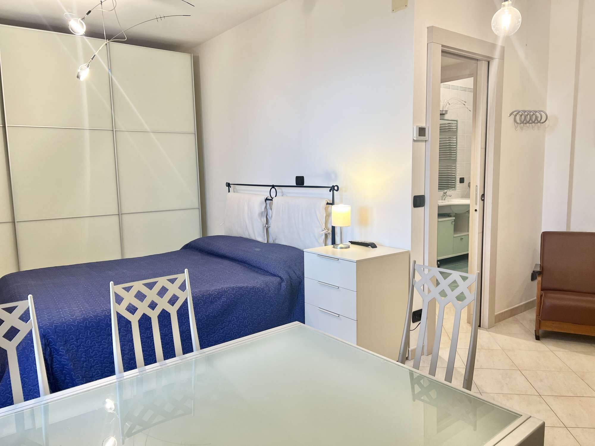 Ein Hotelzimmer mit Bett, Schreibtisch, Stuhl, Tisch und einem durch eine offene Tür einsehbarer Badezimmer.