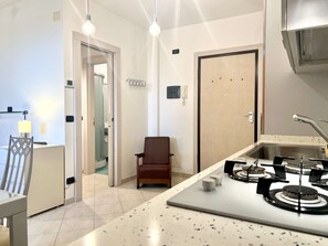 A modern kitchen with a gas stove, a chair, and a door leading to a bathroom. - A BALCONY ON THE PIAZZA OF THE PALIO (Siena)