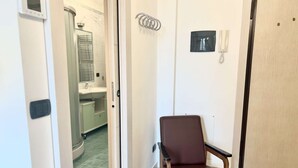 Ett rum med en brun stol, en vit dörr och utsikt över ett badrum med handfat och spegel.