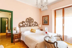 Ein Hotelzimmer mit einem großen Bett, einer Chandelüster, einem Gemälde und Blick ins Freie.
