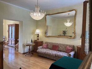 Ein Wohnzimmer mit einer Kristallleuchter, einem großen Spiegel, einem Sofa und einem Tisch mit Blumen.