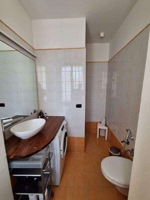 Un baño moderno con lavamanos grande, lavadora, inodoro y cabina de ducha.