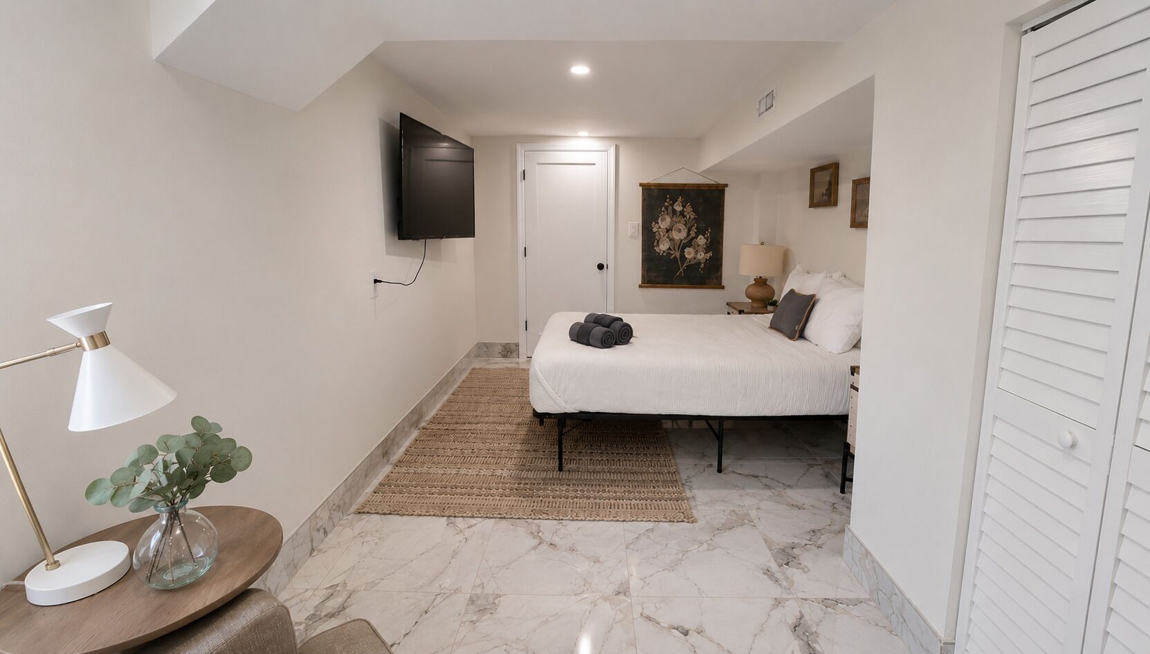 Une chambre à coucher comprenant un lit, un téléviseur à écran plat fixé au mur, une table de chevet avec une lampe et une porte.