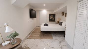 Quarto com cama, televisão de tela plana na parede, mesa de cabeceira com abajur e uma porta.