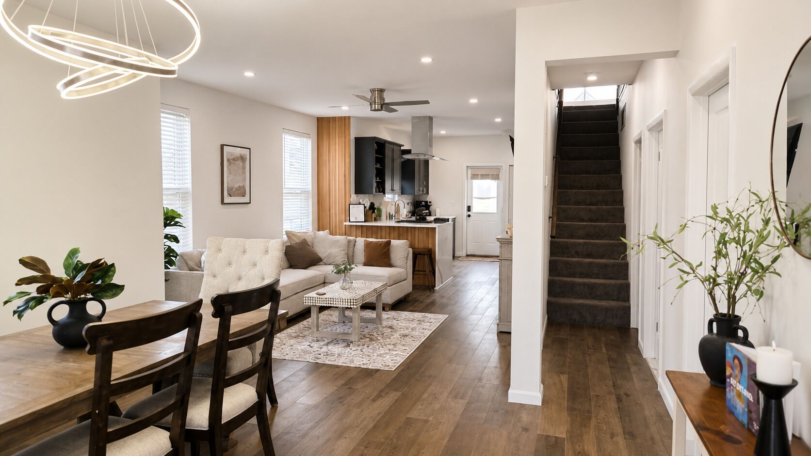 A modern living room with a dining area, kitchen, and staircase.
