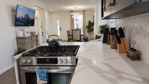 A modern kitchen with a stainless steel stove, oven, and a flat-screen TV mounted on the wall. - The Cornerstone | Historic Coastal Getaway (Atlantic City)