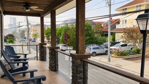 A covered outdoor seating area with chairs and a view of parked cars and houses. - The Cornerstone | Historic Coastal Getaway (Atlantic City)
