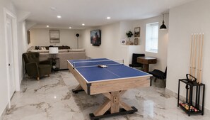 Una habitación con mesa de ping pong, sofá, mesa de centro y soporte para billar.