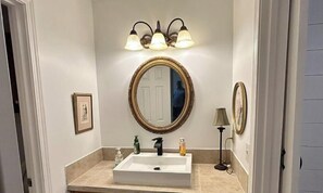 A bathroom with a white sink, a mirror with a gold frame, and a wall-mounted light fixture. - Peaceful retreat in friendly Lilburn, Georgia (Lilburn)