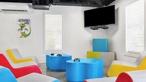 Una stanza con sedute colorate, una TV a schermo piatto e un cartello che segnala un'area attività.