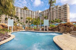 A hotel pool area with a clock, palm trees, and a large building in the background. - 2 Bedroom Villa at Marriott Aruba Surf Club (Noord)