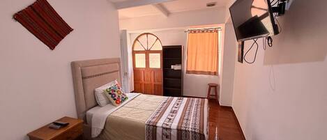 Un dormitorio con cama, mesita de noche, televisor, armario y ventana con cortinas.