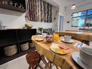 A dining area with wooden tables and chairs, a variety of textiles on the wall, and a window with a view. - Hotel Choqechaka  (Cusco)