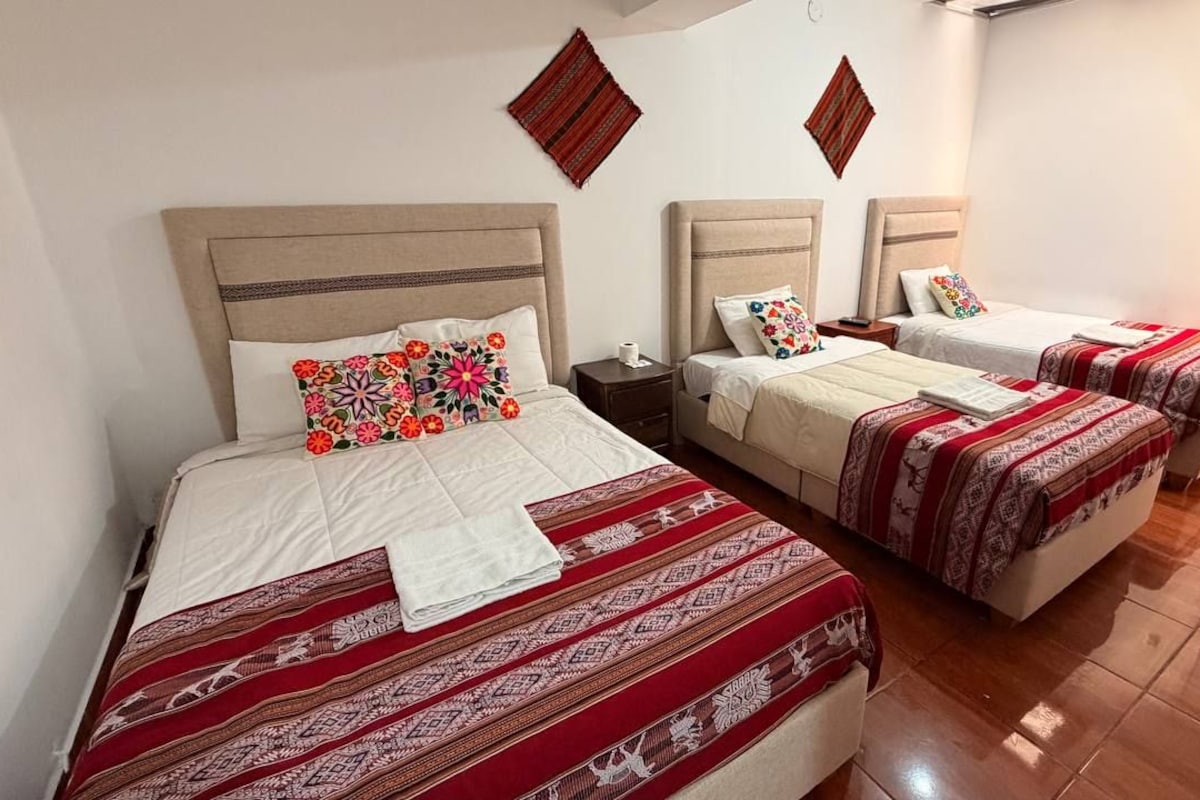 A hotel room with three beds, each with a patterned bedspread and pillows.