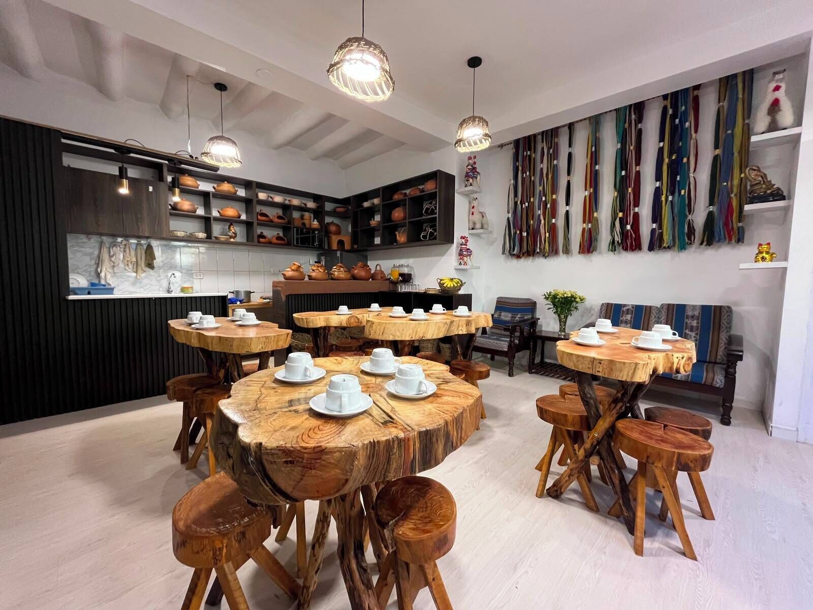 A modern kitchen with wooden tables and stools, a variety of kitchenware, and a wall of colorful textiles.