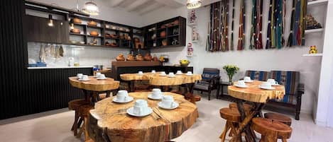 A modern kitchen with wooden tables and stools, a variety of kitchenware, and a wall of colorful textiles.