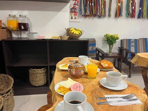 Un desayuno con una mesa de madera, una taza de café, una tetera, un cesto de plátanos y diversas opciones para el desayuno.